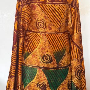 May include: A fabric length featuring a batik-style pattern in shades of deep brown, golden yellow, and forest green. The design consists of horizontal bands with geometric shapes, including triangles, stripes, circles, and star-like motifs.