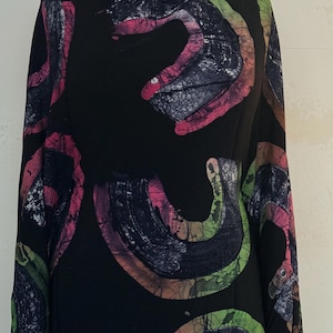 May include: A black fabric featuring a repeating batik-style pattern of curved, crescent-shaped motifs. The shapes are filled with vibrant gradients of pink, lime green, and orange, accented by a dark, crackled texture throughout the design.