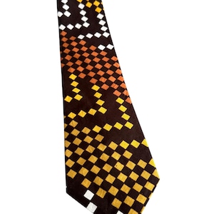 Peut inclure: Une cravate présentant un fond marron foncé avec un motif géométrique composé de petits carreaux carrés dans des tons jaune, orange et blanc. Les carrés sont disposés selon un design en dégradé qui traverse la surface du tissu.