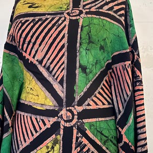 May include: A fabric featuring a geometric batik pattern in black, green, yellow, and coral pink. The design consists of intersecting black lines forming circular centres and triangular sections filled with either solid colours or parallel striped lines.