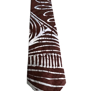 May include: A necktie featuring a dark brown background with a white batik-style pattern consisting of abstract lines, curved shapes, and linear segments. The fabric displays a distinct wax-resist texture throughout the surface of the pointed accessory.