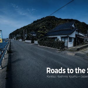 以下が含まれることがあります： 日本の九州、糸島市唐津にある海岸沿いのアスファルト道路。金属製のガードレールと水辺に隣接しています。日本語のテキストと赤い矢印が描かれた標識が立っています。右下には「Roads to the Sea」という白いテキストが印刷されています。