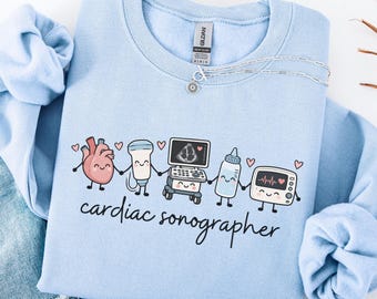 May include: A light blue crewneck sweatshirt featuring a graphic of a cartoon heart, ultrasound probe, ultrasound machine, baby bottle, and heart monitor holding hands. The text "cardiac sonographer" is printed below the graphic.