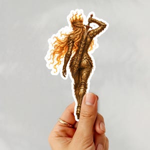 May include: A die-cut sticker featuring a figure in ornate gold armour and a crown of flames, viewed from behind. The figure has long, flowing orange hair and holds a sword upright against their back, rendered in detailed metallic tones.