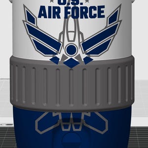 May include: A white and blue cylindrical cooler featuring the text U.S. AIR FORCE in dark blue letters above a stylized graphic of a fighter jet. The cooler has a wide, textured grey band around the middle and a solid dark blue base section.
