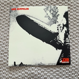 May include: Led Zeppelin album cover featuring a black and white image of the Hindenburg airship in mid-air. The band's name is in red at the top, with the Atlantic Records logo in the bottom right corner.