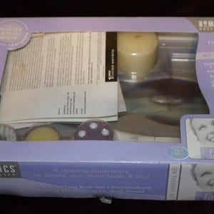 May include: A HoMedics Body Basics Spa Therapy Kit in a light purple rectangular box with a clear plastic window. The kit includes a facial brush with three attachments, a storage bag, a relaxation CD, a vanilla scented candle, a mirror, and a gel mask.