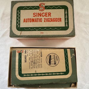 May include: Vintage Singer Automatic Ziggzagger sewing machine attachment box. The box is beige with green trim and text. The top of the box reads "SINGER AUTOMATIC ZIGZAGGER". The bottom box contains a pamphlet.