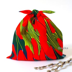 May include: A red fabric gift bag with green and yellow abstract patterns. The bag is tied with a knot at the top and has a white tag with the word "@suika" on it.