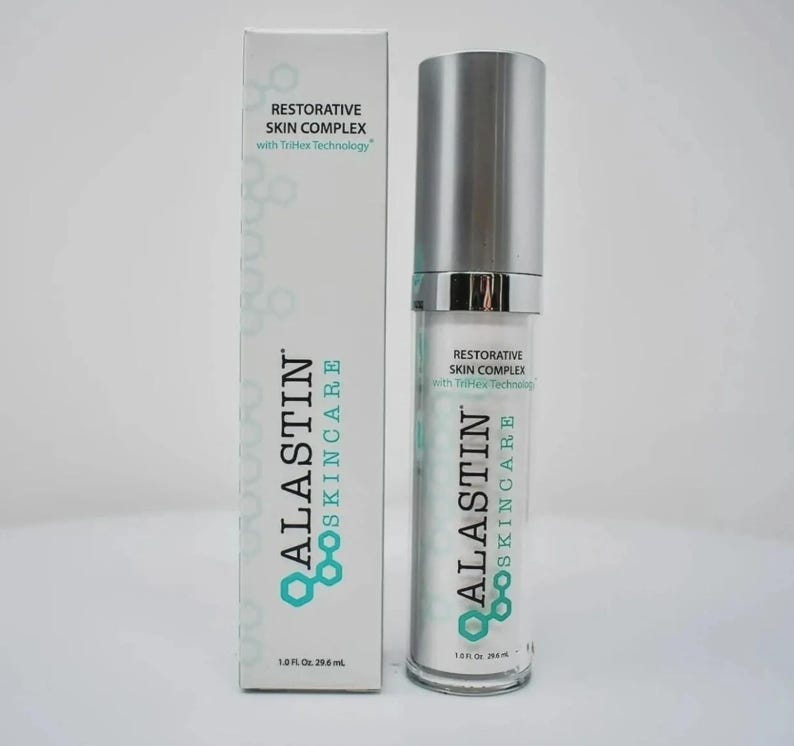 Op de afbeelding: Een witte doos en een heldere fles van Alastin Skincare Restorative Skin Complex. De doos en de fles hebben hetzelfde ontwerp, met de merknaam en productinformatie in zwart en blauwgroen. De fles bevat 29,6 ml.