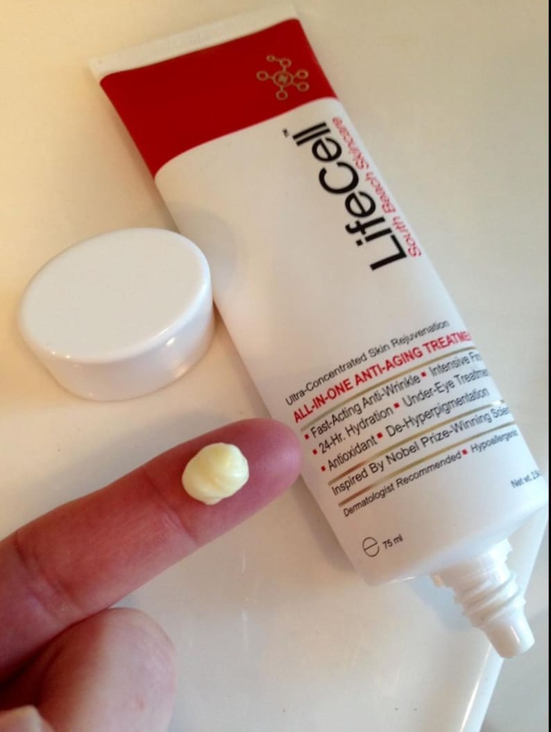 May include: A white and red tube of LifeCell South Beach Skincare All-In-One Anti-Aging Treatment with a detached white cap. The tube features text detailing benefits like anti-wrinkle and hydration, with a net volume of 75 ml printed on it.