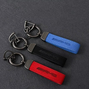 Puede incluir: Tres llaveros con una correa rectangular que presenta el logotipo de AMG grabado en la superficie. Cada llavero incluye una anilla metálica oscura y un accesorio de anilla más pequeño. Las correas están disponibles en azul, negro y rojo.