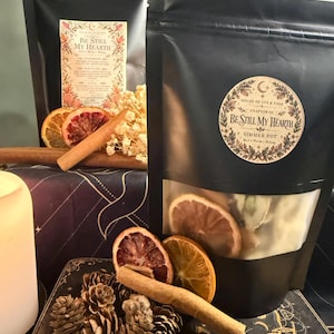 May include: Two black pouches labelled Be Still My Hearth, Chapter III, House of Ivy & Sage. The pouches contain dried fruit slices, cinnamon sticks, and botanicals. One pouch features a circular label, while the other has a rectangular label.