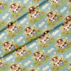 May include: A light blue fabric featuring a repeating pattern of cartoon cows with brown spots. Each cow stands on a small green patch of grass with red mushrooms, holding a grey bucket filled with white sudsy liquid against a sky background.