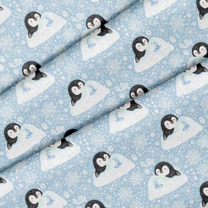 May include: A light blue fabric featuring a repeating pattern of black and white penguins resting on white icebergs, interspersed with white snowflakes and small blue fish icons, creating a winter-themed textile design.