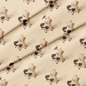 May include: A light beige fabric featuring a repeating pattern of cartoon cows with brown spots and orange muzzles. Some cows have a small blue bird perched on their heads. The textile has a visible woven texture throughout the entire surface.