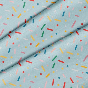 Peut inclure: Un tissu bleu clair orné d'un motif répétitif de vermicelles colorés dans des tons rouge, jaune, vert, rose, blanc et bleu foncé. Le design se compose de petits points et de courtes lignes rectangulaires fines dispersées sur la surface.