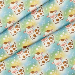 May include: A fabric print featuring a repeating pattern of cartoon cows with brown spots and closed eyes. The background is a soft gradient of yellow, green, and blue, decorated with small white line-drawn flowers and leaves throughout the design.