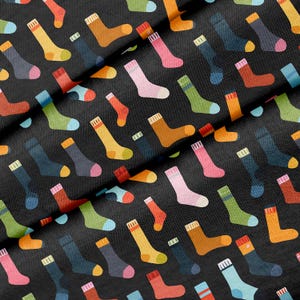 Könnte beinhalten: Ein schwarzer Stoff mit einem sich wiederholenden Muster aus Socken in verschiedenen Unifarben wie Gelb, Orange, Pink, Grün, Blau und Braun. Jede Socke ist mit einem gerippten Bündchen sowie einer abgesetzten Ferse und Spitze versehen und verstreut angeordnet.