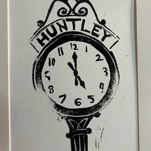 May include: A black and white linocut print on paper featuring a stylized street clock with the word HUNTLEY arched above the clock face. The clock shows the time at approximately 11:25. The text HUNTLEY CLOCK is written in the bottom left corner.