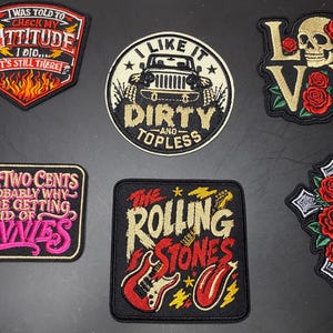 May include: Six embroidered patches featuring various designs: a shield with flames and text, a circular off-white patch with a vehicle and text, a skull with roses, a rectangular patch with pink text, a Rolling Stones logo, and a cross with roses.