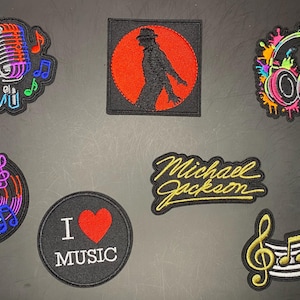 May include: A collection of seven embroidered patches featuring music-themed designs including a microphone, a silhouette of a dancer in a red circle, colorful headphones, a vinyl record, a Michael Jackson signature, an I Love Music patch, and a treble clef.