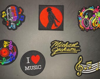 Könnte beinhalten: Eine Sammlung von sieben bestickten Aufnähern mit Musikmotiven, darunter ein Mikrofon, die Silhouette eines Tänzers in einem roten Kreis, bunte Kopfhörer, eine Schallplatte, der Schriftzug Michael Jackson, ein I Love Music Aufnäher und ein Violinschlüssel.