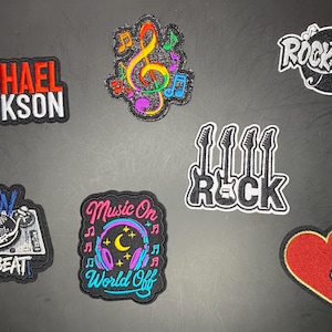 May include: A collection of six embroidered patches featuring music themes: Michael Jackson text, a colorful treble clef, a Rock N Roll emblem, a turntable with Spin The Beat text, headphones with Music On World Off text, and a red heart with a gold note.