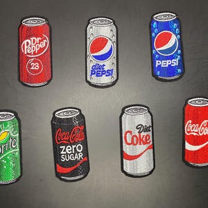 May include: A collection of seven embroidered patches shaped like soda cans. The designs include red Dr. Pepper, silver Diet Pepsi, blue Pepsi, green Sprite, black Coca-Cola Zero Sugar, silver Diet Coke, and red Coca-Cola, each with brand logos.
