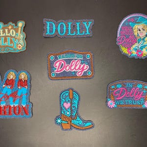 Peut inclure: Sept écussons brodés sur le thème de Dolly Parton. Les motifs incluent un écusson Hello Dolly, un écusson au nom de Dolly, un portrait circulaire, une plaque d'immatriculation Dolly, trois figurines Dolly, une botte de cow-boy et In Dolly We Trust.