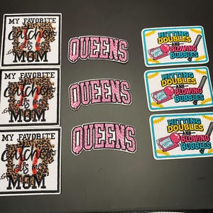 Könnte beinhalten: Drei quadratische Aufnäher mit Leopardenmuster und Baseball-Grafik mit der Aufschrift MY FAVORITE catcher calls me MOM, drei bogenförmige Aufnäher mit der Aufschrift QUEENS in Pink und drei rechteckige Aufnäher mit HITTING DOUBLES AND BLOWING BUBBLES.