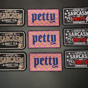 Puede incluir: Nueve parches rectangulares bordados dispuestos en tres columnas. La columna izquierda presenta parches negros con texto de estampado de leopardo Raised on Sarcasm & Sweet Tea. La columna central tiene parches a cuadros rosas y dorados con la palabra petty en azul. La columna derecha muestra parches negros con texto blanco y rojo Fueled by Sarcasm and Petty Thoughts con un icono de rayo y bola.