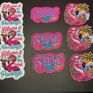 May include: Three embroidered patches featuring a pink flamingo wearing heart-shaped sunglasses and holding a cocktail, with the text Blame it on the Drink Package. Three patches with the word SALTY in blue, and three flamingo patches.