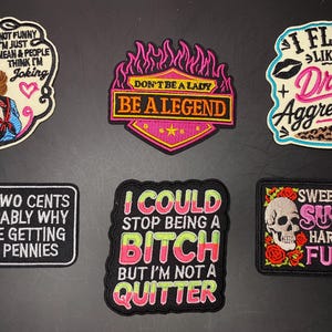 May include: Six embroidered patches with various designs and text. Top row: a woman with the text I'M REALLY NOT FUNNY, a shield with DON'T BE A LADY BE A LEGEND, and text I FLIRT LIKE I DRINK AGGRESSIVELY. Bottom row: text YOUR TWO CENTS, I COULD STOP BEING A BITCH, and a skull with SWEET AS SUGAR HARD AS FUCK.