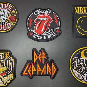 May include: Six embroidered fabric patches featuring music-themed designs. The patches include a Live Loud microphone, a red tongue logo, a yellow Nirvana smiley face, a Led Zeppelin airship, a Def Leppard logo, and a Fleetwood Mac moon design.