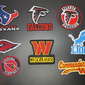 May include: A collection of eight embroidered NFL team patches featuring the Houston Texans, Atlanta Falcons, Arizona Cardinals, Detroit Lions, and Washington Commanders logos in various shapes, colors, and text designs arranged on a dark surface.