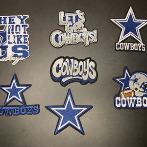 May include: A collection of seven embroidered patches featuring blue and silver Dallas Cowboys themes. Designs include a star, a football helmet, and text reading "THEY NOT LIKE US," "LET'S GO COWBOYS!," and "COWBOYS" in various stylized fonts.
