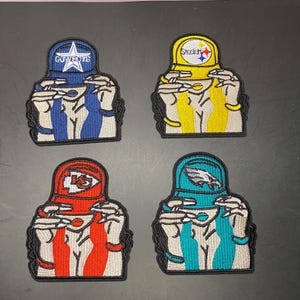 May include: Four embroidered patches featuring figures wearing sports team caps. The top left patch is blue with a Cowboys logo, top right is yellow with a Steelers logo, bottom left is red with a Chiefs logo, and bottom right is teal with an Eagles logo.