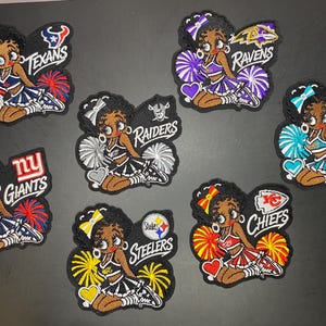 May include: Seven embroidered patches featuring the cartoon character Betty Boop dressed as a cheerleader in various NFL team colors. Each patch includes the team name and logo, such as Texans, Ravens, Dolphins, Giants, Raiders, Steelers, and Chiefs.