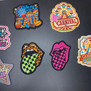May include: A collection of seven embroidered patches featuring various designs including a ferris wheel, carnival themes, lips with checkered tongues, a star with the text Howdy Darlin, and a patch with the text Your Two Cents Is Probably Why They're Getting Rid Of Pennies.