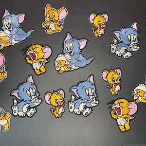 May include: A collection of embroidered fabric patches featuring the cartoon characters Tom and Jerry in various poses. The patches display blue cats and yellow mice with pink ears, some showing the cat interacting with the mouse or the mouse alone.