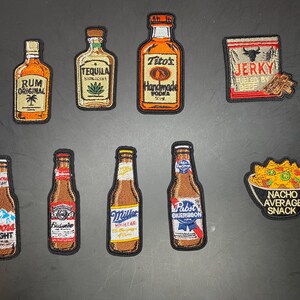 May include: A collection of embroidered patches featuring various beverage bottles including Rum, Tequila, Tito's Vodka, Coors Light, Budweiser, Miller High Life, and Pabst Blue Ribbon, alongside a Jerky package and a bowl of nachos labeled Nacho Average Snack.