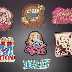 Puede incluir: Una colección de seis parches bordados con imágenes y texto de Dolly Parton. Los diseños incluyen un retrato con sombrero de vaquero, un marco de cuerda con el texto RAISED ON DOLLY, un letrero rosa de HELLO DOLLY, tres figuras, un retrato de Larger Than Life y un parche con el nombre DOLLY.