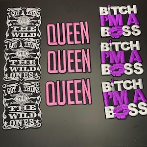 Peut inclure: Trois écussons brodés avec le texte I GOT A THING FOR THE WILD ONES en blanc sur noir, trois écussons avec le mot QUEEN en rose sur noir, et trois écussons avec le texte BITCH I'M A BOSS en blanc et violet avec une icône de lèvres.