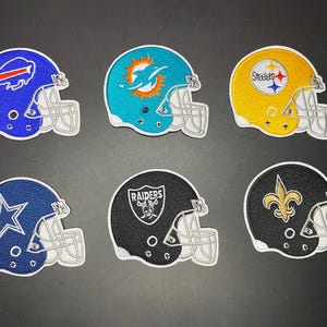 May include: A set of six embroidered patches shaped like football helmets, featuring the logos of the Buffalo Bills, Miami Dolphins, Pittsburgh Steelers, Dallas Cowboys, Las Vegas Raiders, and New Orleans Saints in their respective team colors.