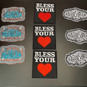 May include: Nine embroidered patches arranged in three columns. The left column features three brown glittery patches with the text "Somebody's PROBLEM" in blue. The center column has three black square patches with "BLESS YOUR" and a red heart. The right column shows three black and white patches with the text "GOOD VIBES" in a decorative frame.