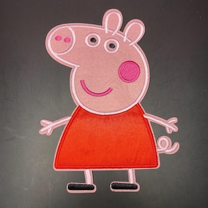 May include: An embroidered fabric patch featuring a cartoon pig character with light pink skin, a bright red dress, and black shoes. The character has two eyes, a snout with two pink nostrils, a pink cheek circle, and a curly tail on the right side.