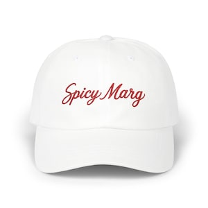 May include: A white baseball cap featuring the text Spicy Marg embroidered in red cursive script across the front panel. The hat has a structured crown, a curved brim, and a button on top, presenting a clean and simple design for headwear.