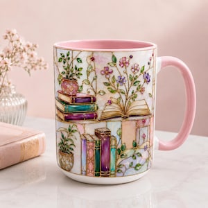 May include: A ceramic mug with a light pink interior and handle, featuring a stained-glass style illustration of stacked books, an open book with blooming flowers, and potted plants in shades of purple, green, blue, and gold on a white base.