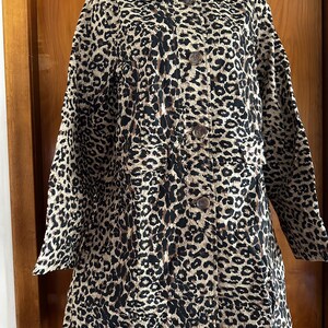 May include: A long-sleeved jacket featuring a prominent black and brown leopard print pattern on a beige background. The jacket includes a classic collar, a front button-down closure with matching buttons, and two horizontal pockets on the front.